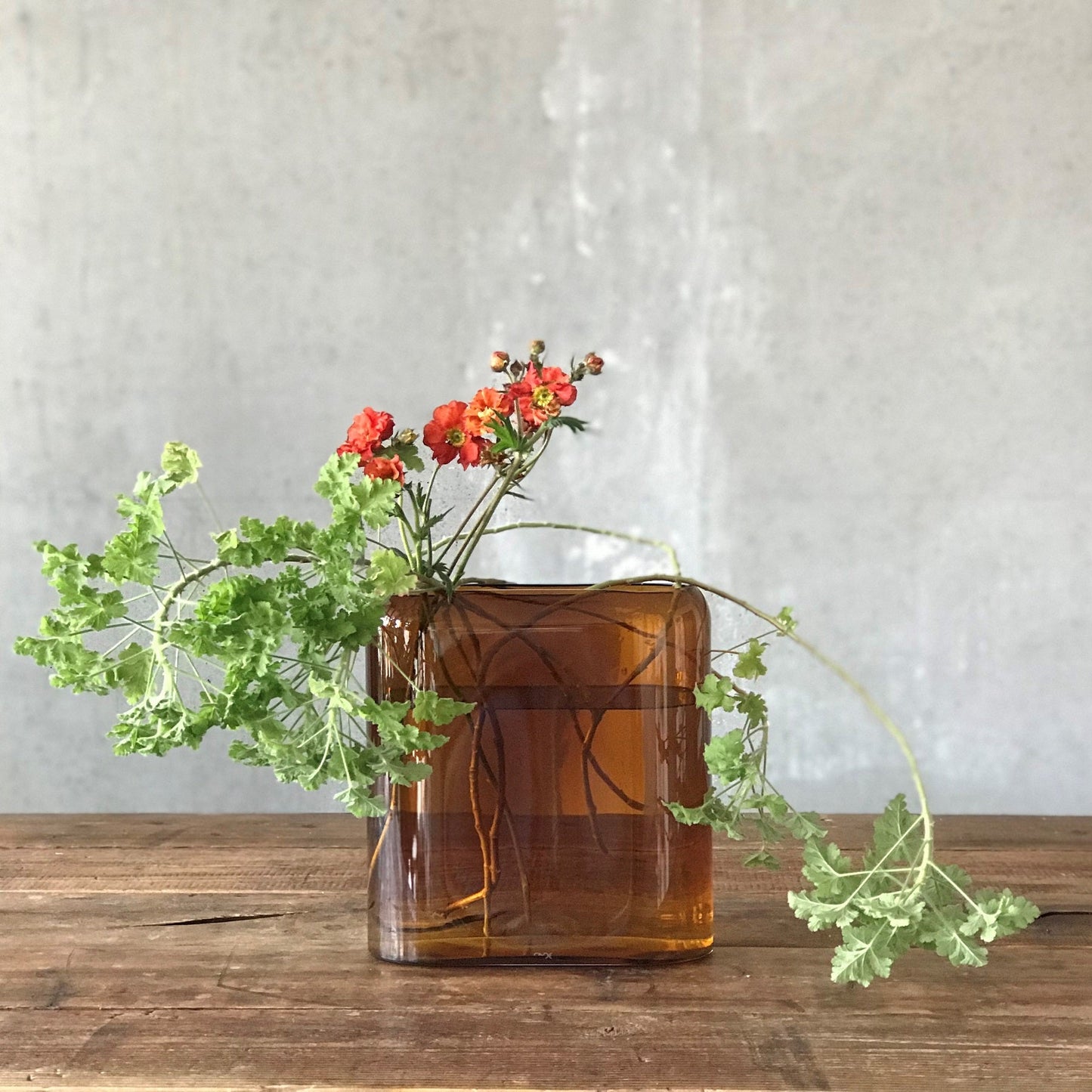Translucent mouth-blown glass vase displaying vibrant floral stems