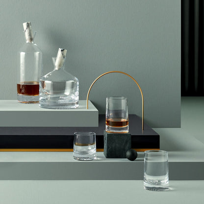 Group collection of NUDE Glass Alba barware including decanters and tumblers on a dark backdrop.