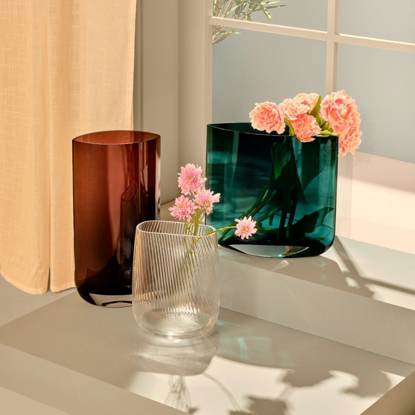 A curated collection of contemporary NUDE Glass vessels including the tall ribbed Opti vase on a stone surface.