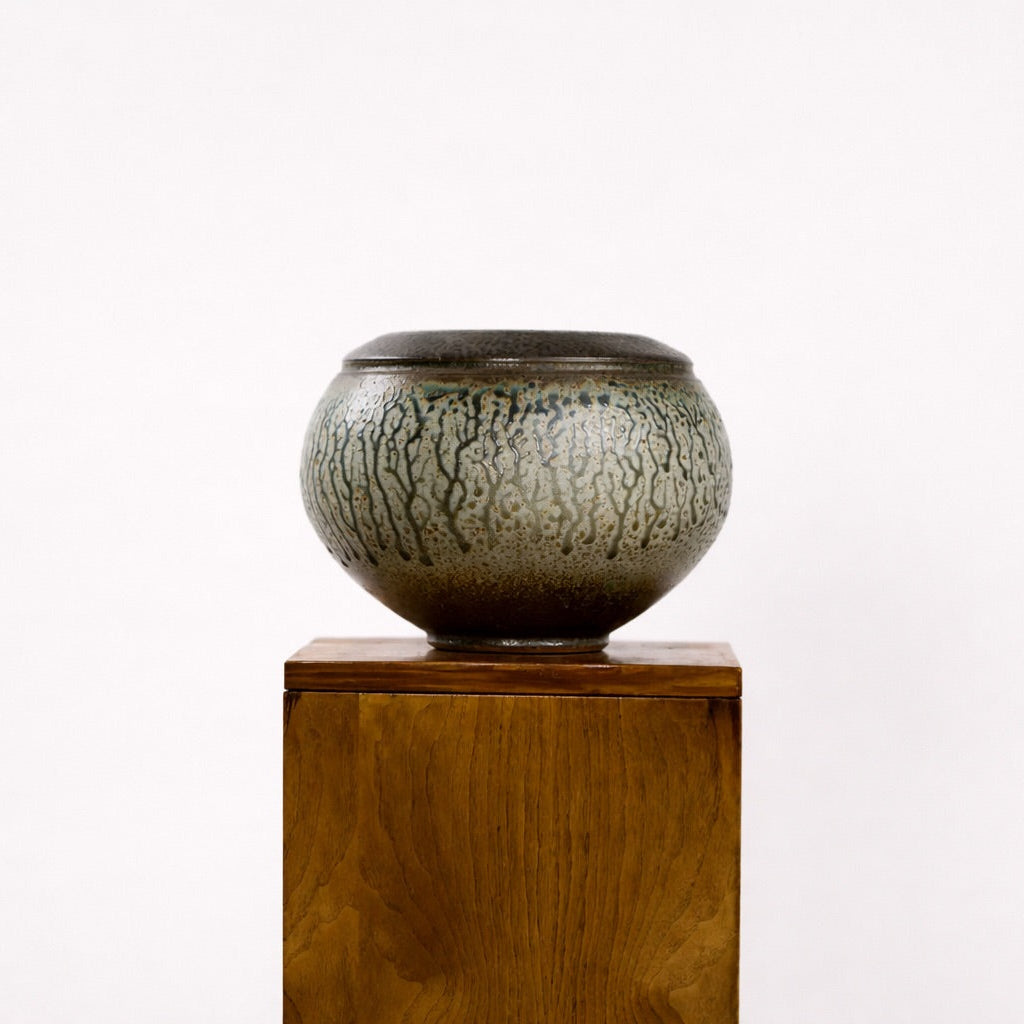 Ceramic bowl with textured surface on a wooden pedestal against a white background