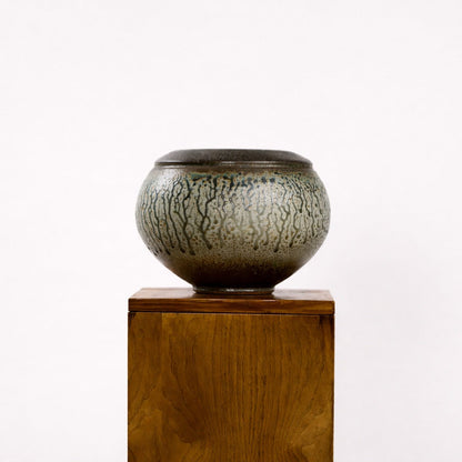 Ceramic bowl with textured surface on a wooden pedestal against a white background