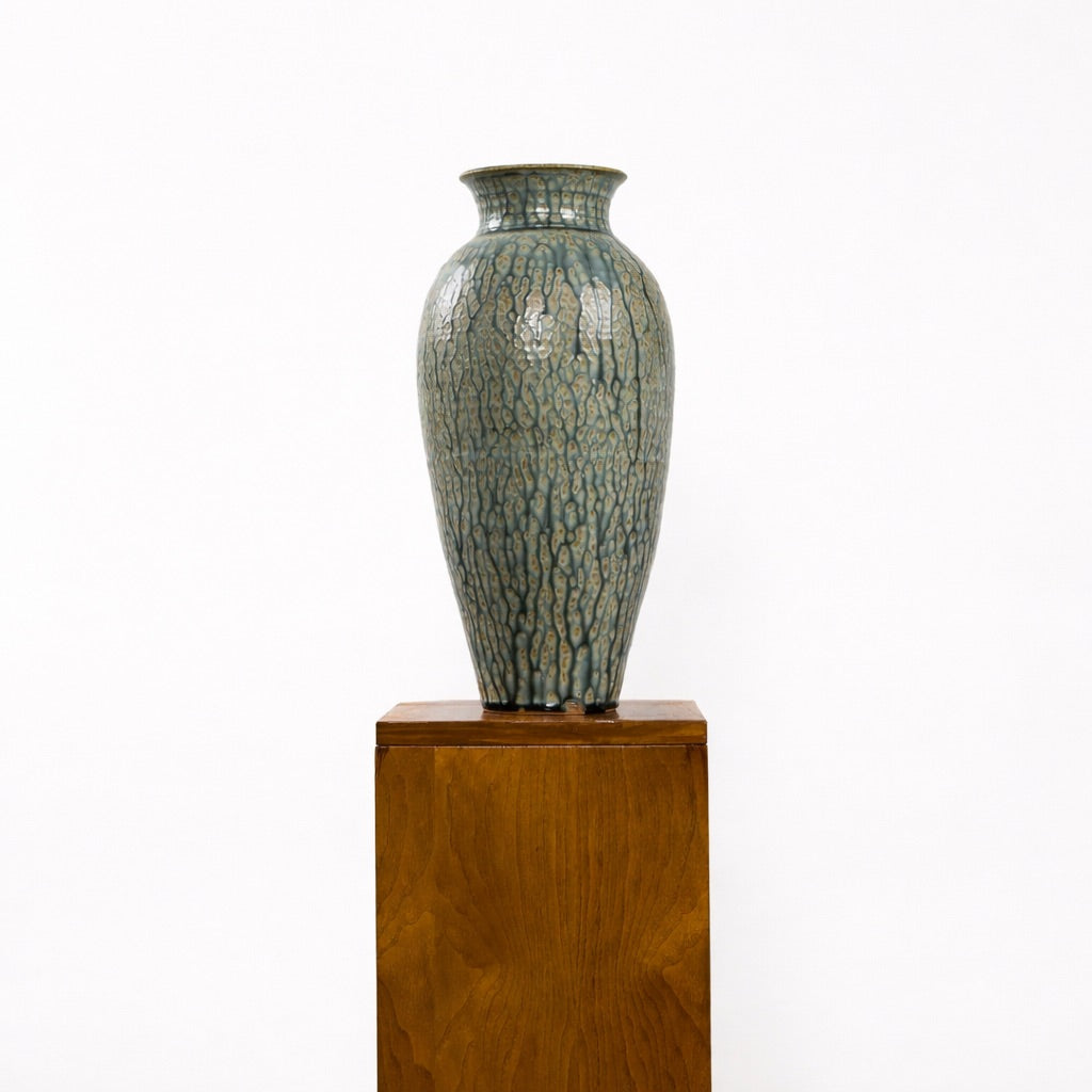Ceramic vase with textured surface on a wooden pedestal against a white background