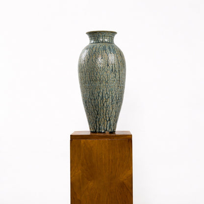 Ceramic vase with textured surface on a wooden pedestal against a white background