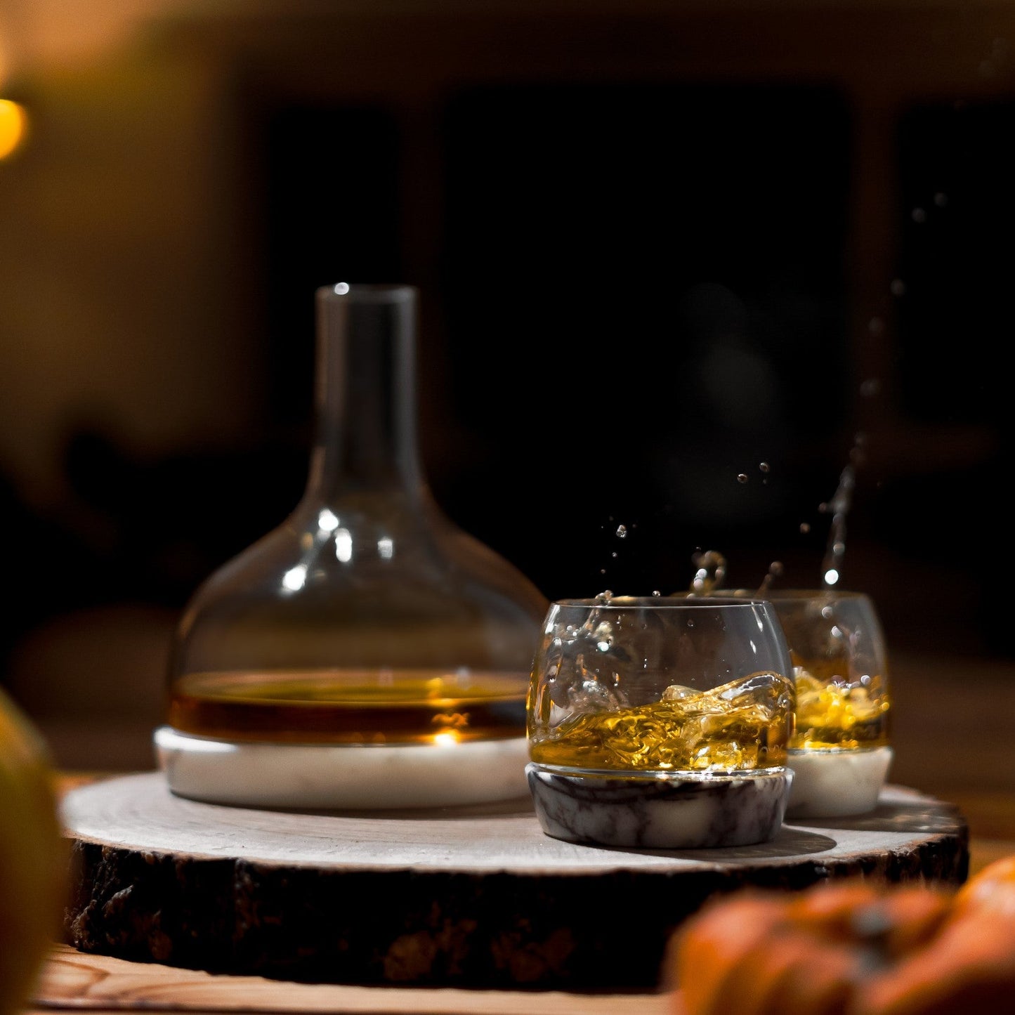 Dynamic styling of the crystal carafe and lowball glasses resting on modern marble stands.