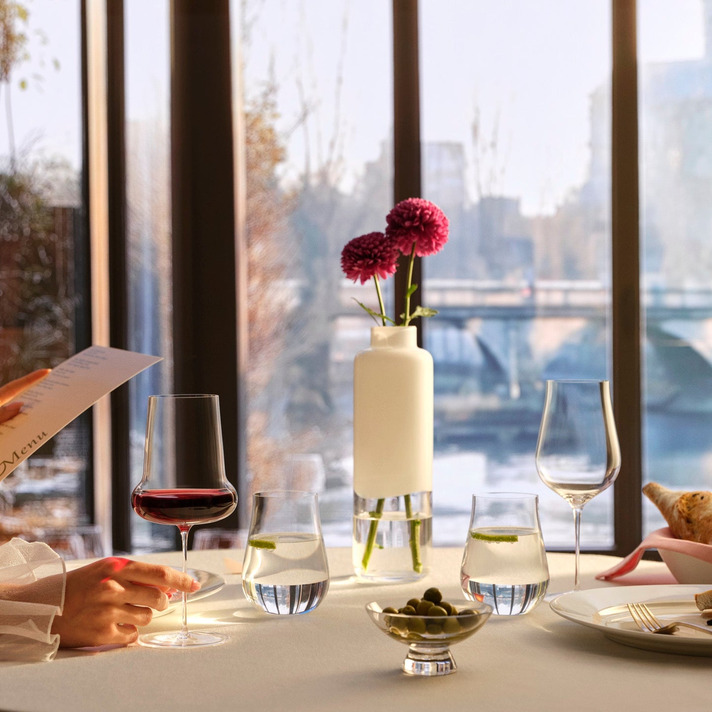 A sophisticated dining table display showcasing a curated collection of NUDE Glass crystal stemware and decorative bowls.