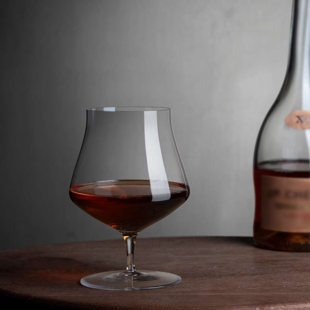 A close-up view of a minimalist crystal cognac glass, highlighting the elegant tapered rim and rounded base.