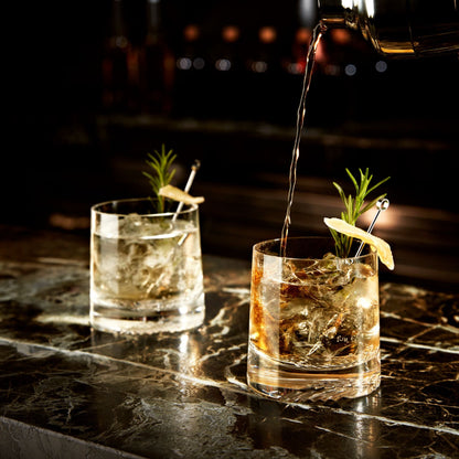 Whisky being poured into a heavy-base crystal Alba tumbler alongside a minimalist decanter.