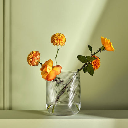 Modernist tall crystal vase styled on a minimalist wooden table, catching light through its textured ripples.