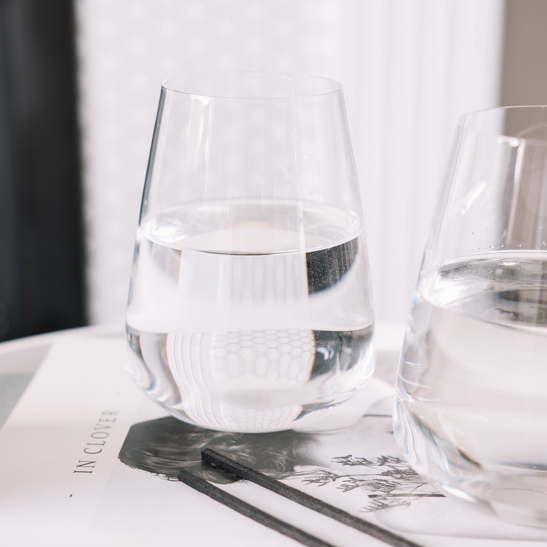 Sleek Stem Zero water glass styled on a contemporary wooden dining table with warm lighting.
