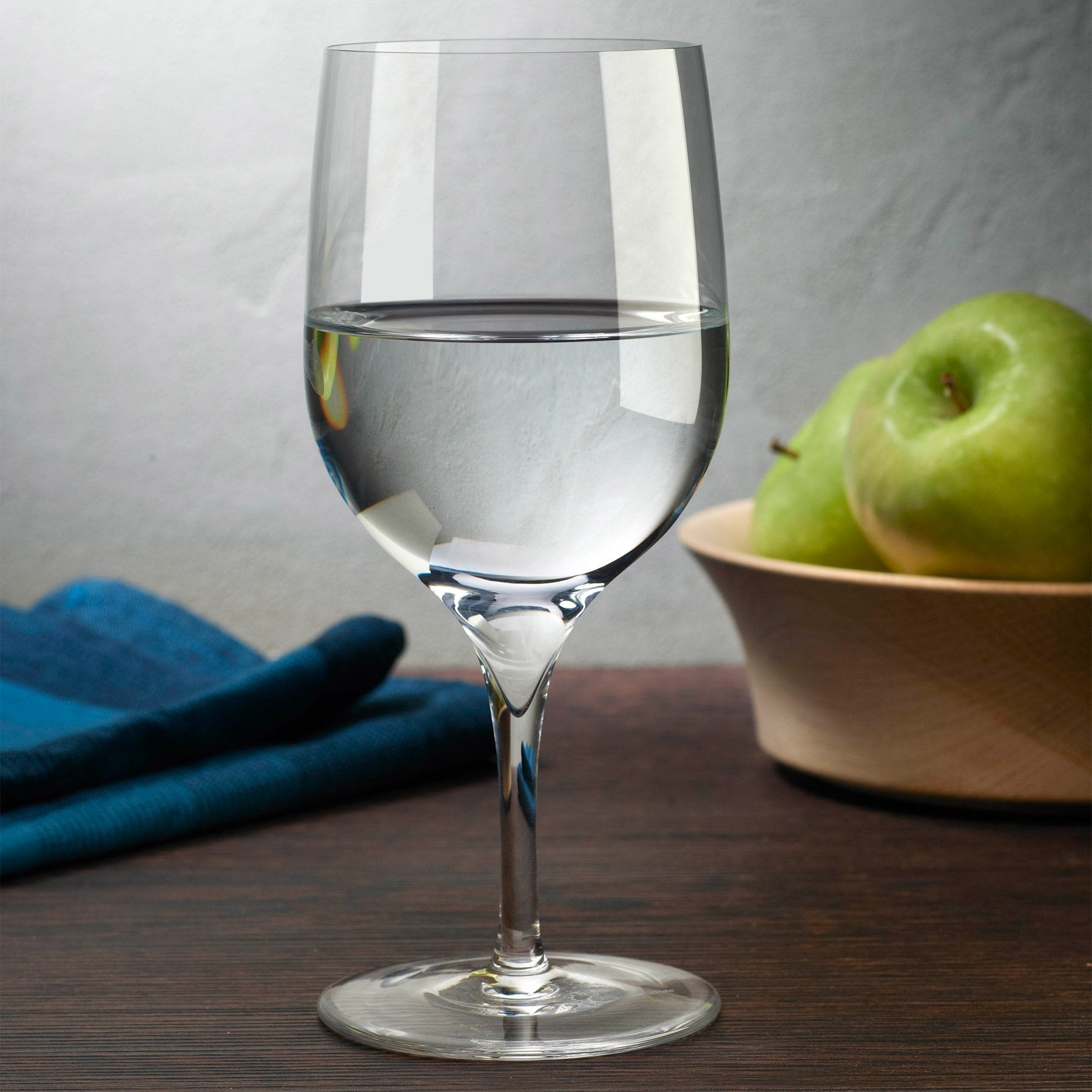 A lifestyle setting featuring the NUDE Glass Dimple crystal water glasses on a modern dining table.