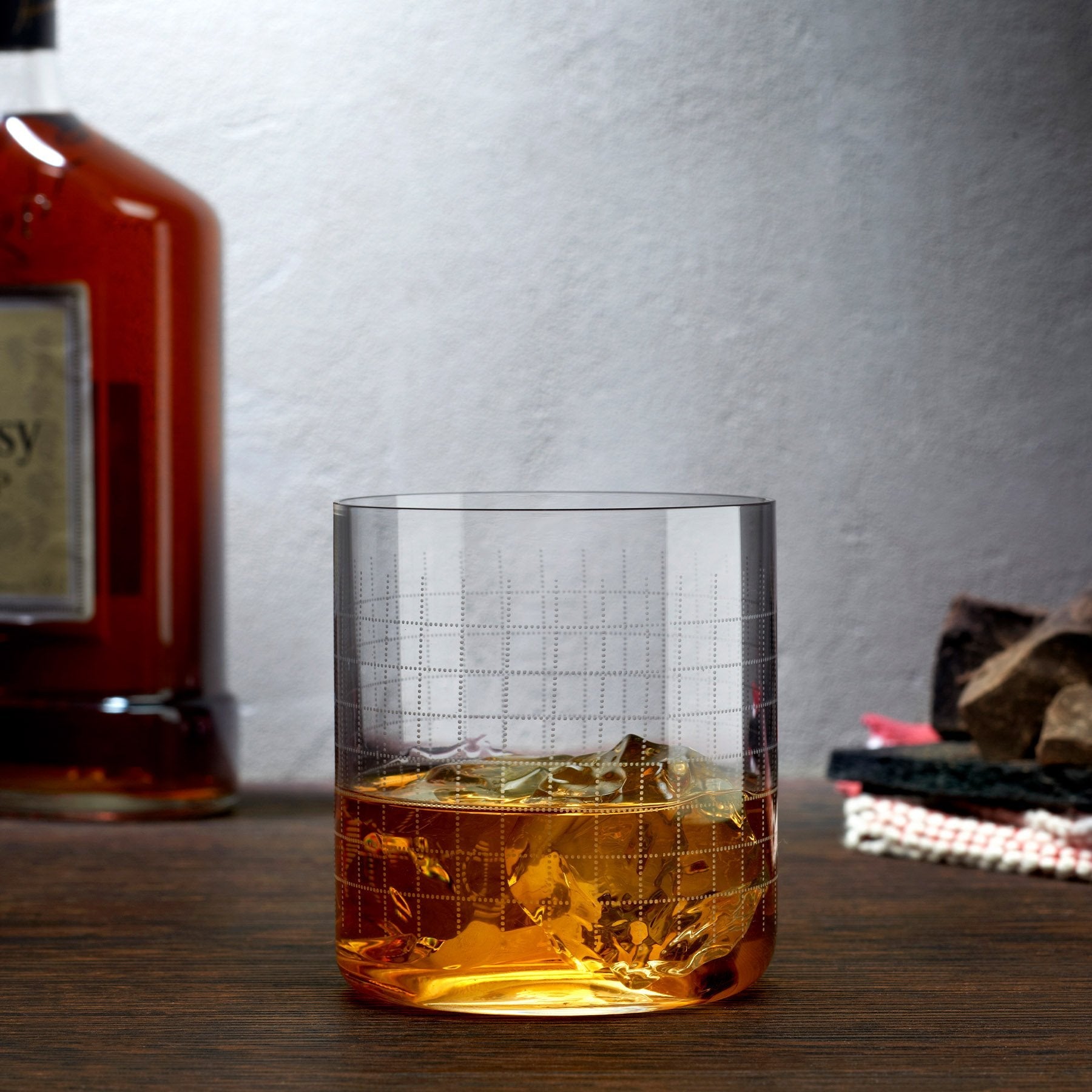 The Finesse Grid crystal whiskey glass styled in a modern bar setting next to elegant decanters and spirits.