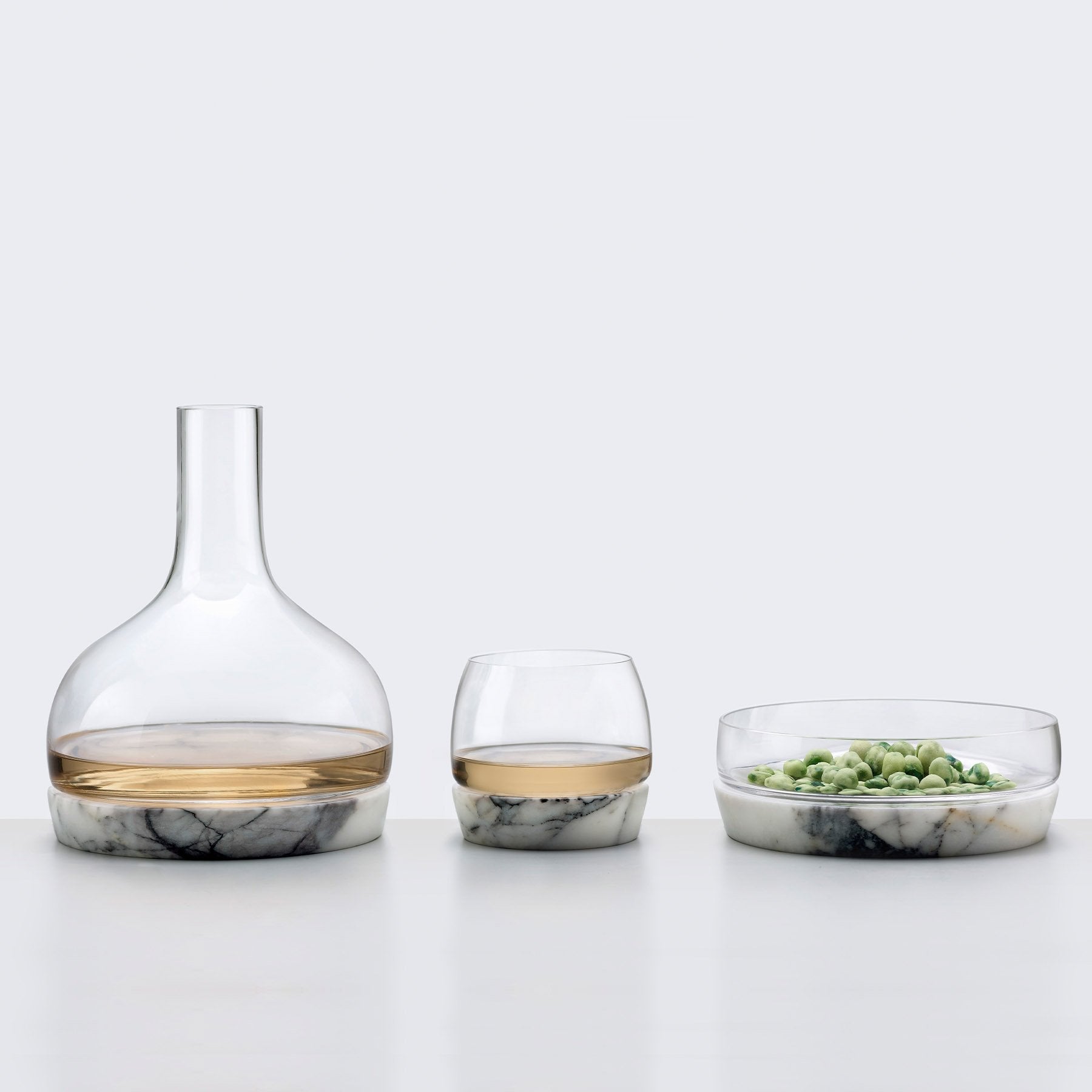 Elegant crystal carafe, matching tumblers, and bowl with marble bases styled on a table.