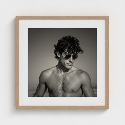 A 20x20 inch monochrome figure study art print set in a light natural wood frame.