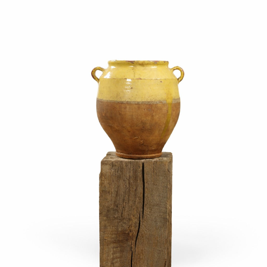 Yellow ceramic vase on a wooden stand against a white background